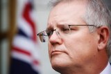 Scott Morrison looks into the distance with an australian flag behind him