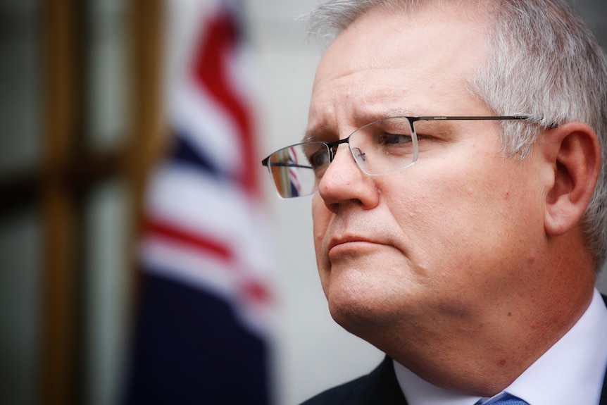 Scott Morrison regarde au loin avec un drapeau australien derrière lui