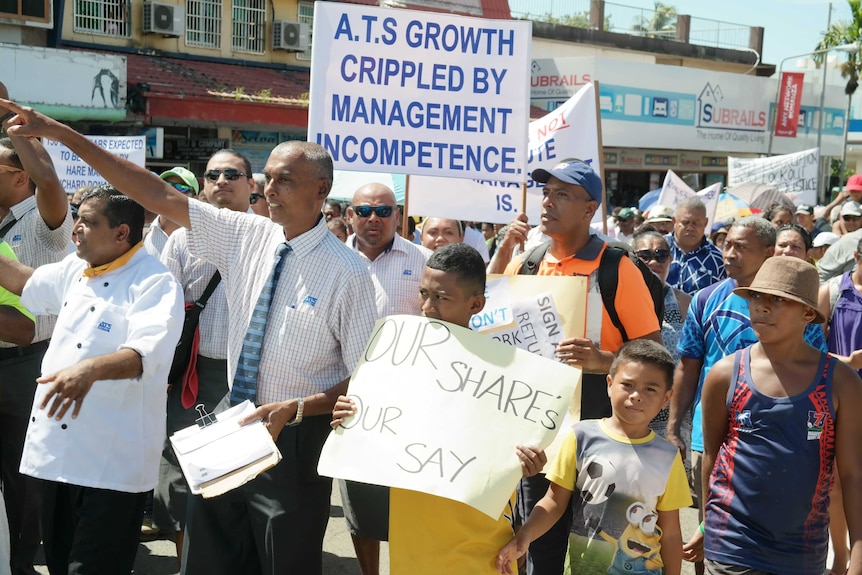 People wearing ATS-branded shirts hold signs and march through a Nadi street.
