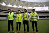 Four ministers wearing high-viz and hard hats stand with hands on hips looking up at the Perth stadium.