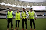 Four ministers wearing high-viz and hard hats stand with hands on hips looking up at the Perth stadium.