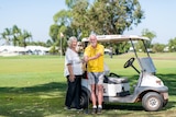 Two elderly people stand next to a golf buggy smiling on a sunny day. 