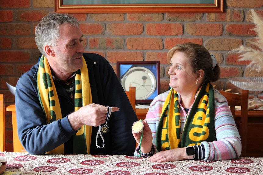 A man and woman look at each other holding medals and wearing football scarves.