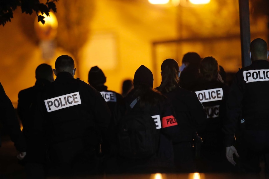French police officers gather together in the street in the evening.