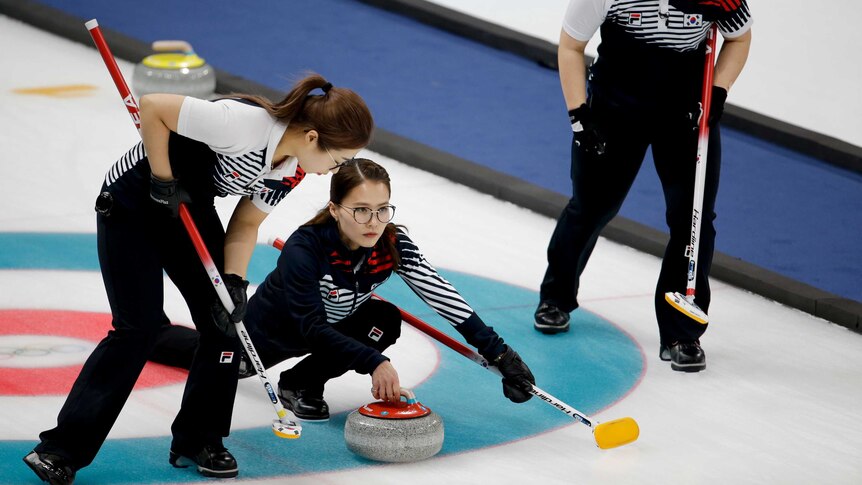 A South Korean curler throws a stone while flanked by two teammates.