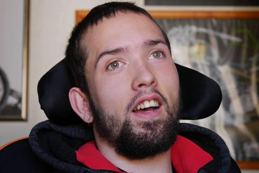 A headshot of a young man with short dark hair and a dark beard sitting in a chair with his head tilted back.