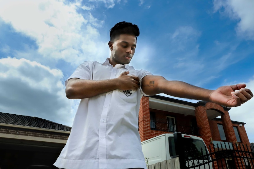 Steve, wearing white short sleeve shirt with black hair, shows a tattoo featuring Chinese symbols on his inner arm