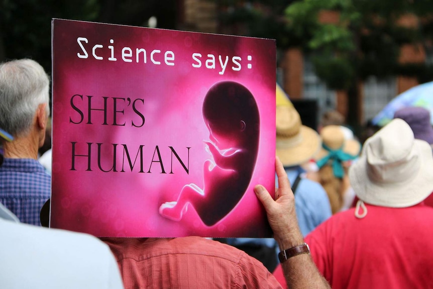 Back view of man holding up 'Science says she's human' sign at an anti-abortion rally on March 18, 2018 in Brisbane's CBD.