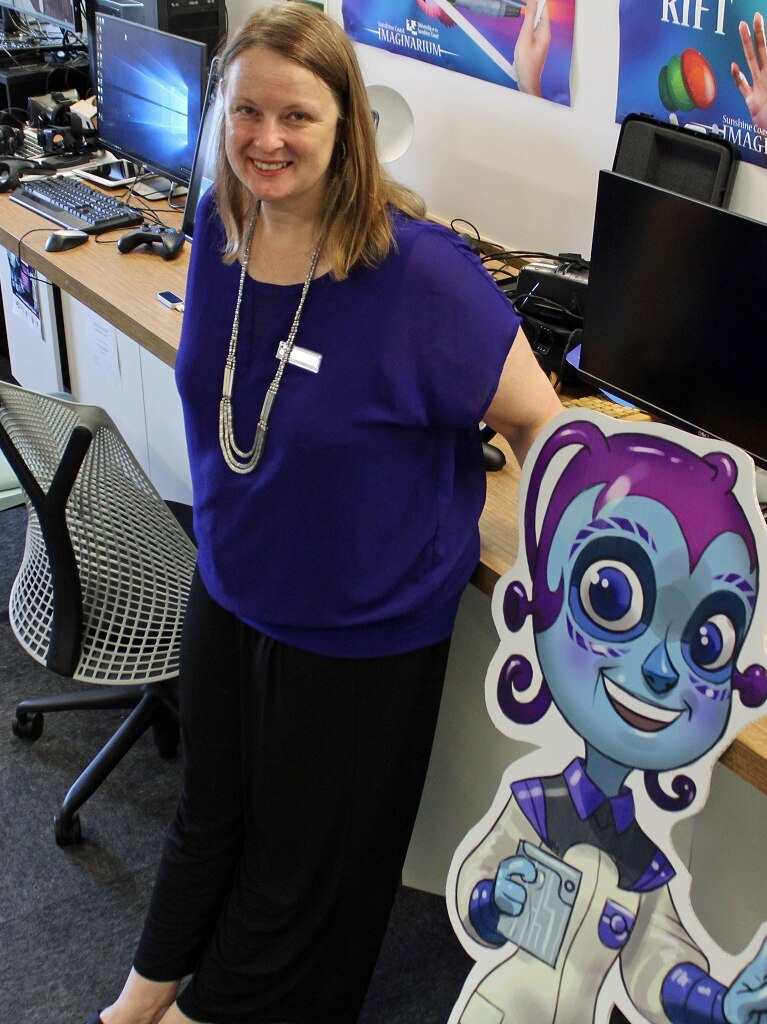 Woman stands smiling in a computer room beside a cardboard cutout of cartoon character