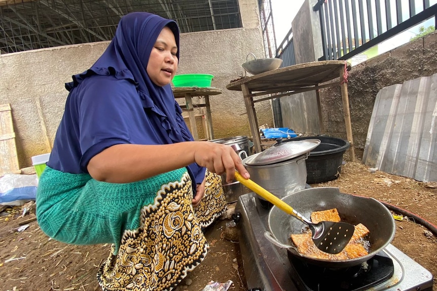 A woman frying food while squatting.