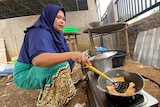 A woman frying food while squatting.