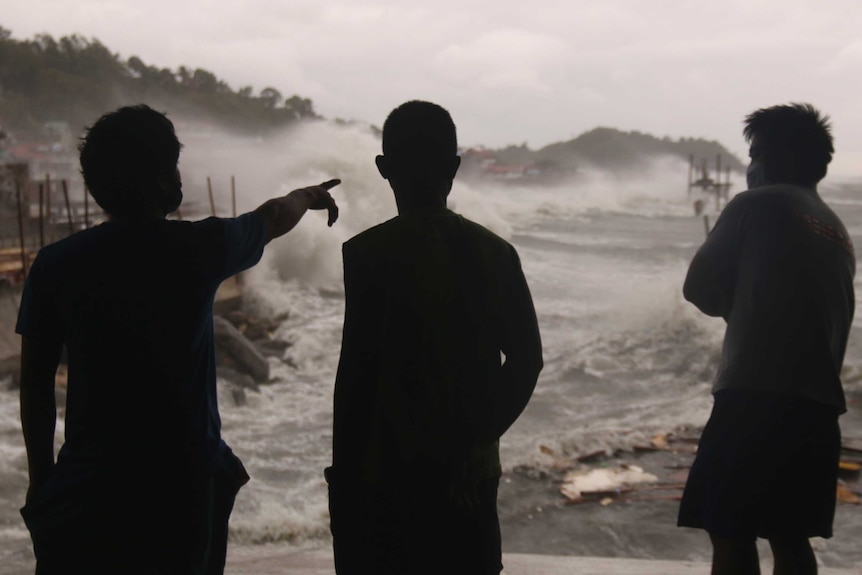 Men watch as strong waves caused by typhoon Vongfong batter the coastline.