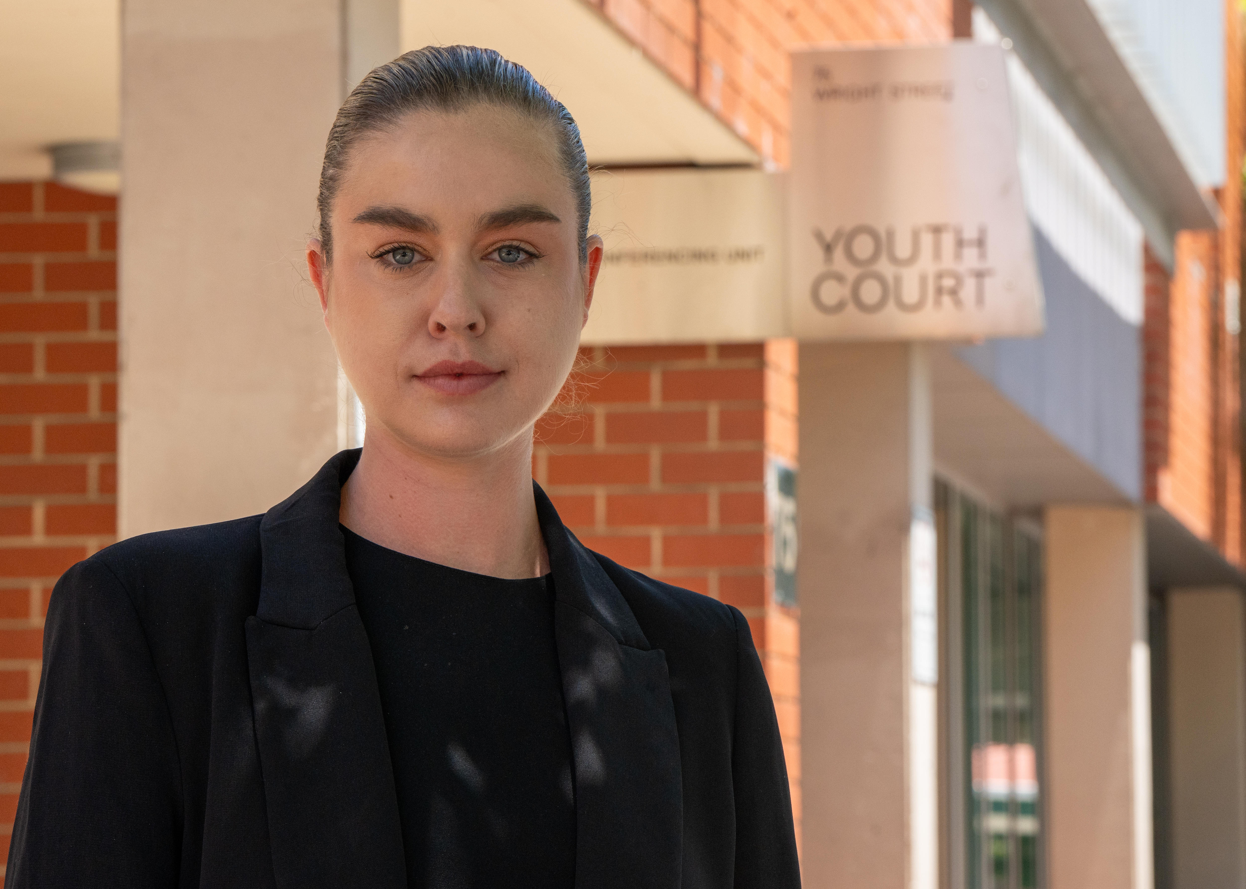 A woman in a black blazer standing in front of a brick building that says Youth Court.