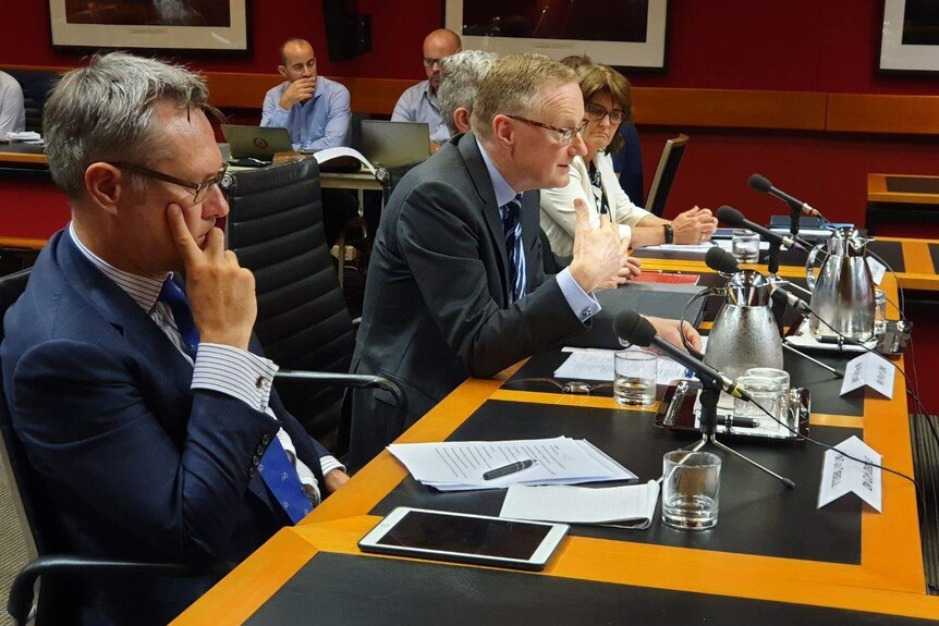 The RBA deputy governor Guy Debelle and governor Philip Lowe sit at a table testifying to Parliament.