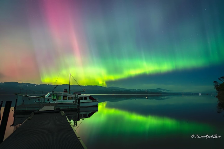An aurora behind a boat on a lake. 