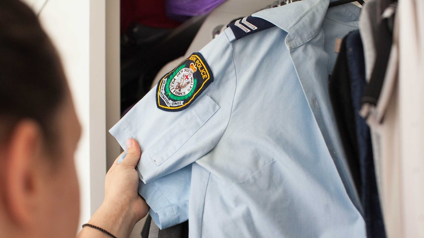 A woman pulls out a NSW police uniform shirt in a wardrobe