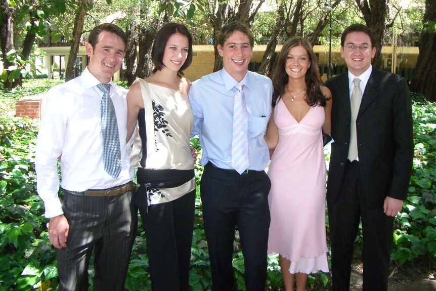 a group of medical students standing arm in arm at their graduation in a garden