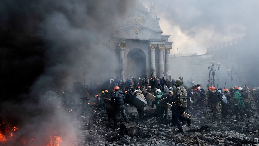 Protesters move across a square past a fire