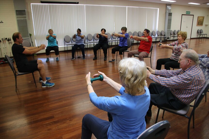 A group of seniors sit in a circle doing arm exercises