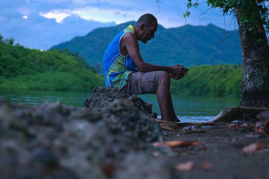 A man sits by the water's edge.