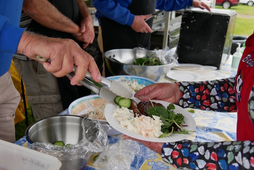 A sausage sizzle and salad on a plate held by a woman.
