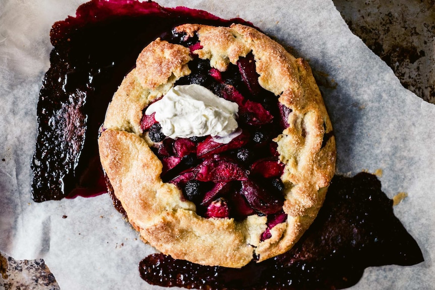Summer galette with stone fruit and blueberries on a baking tray with berry juice oozing out, an easy dessert recipe.
