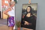 A woman stands looking at a replica of the Mona Lisa painting.
