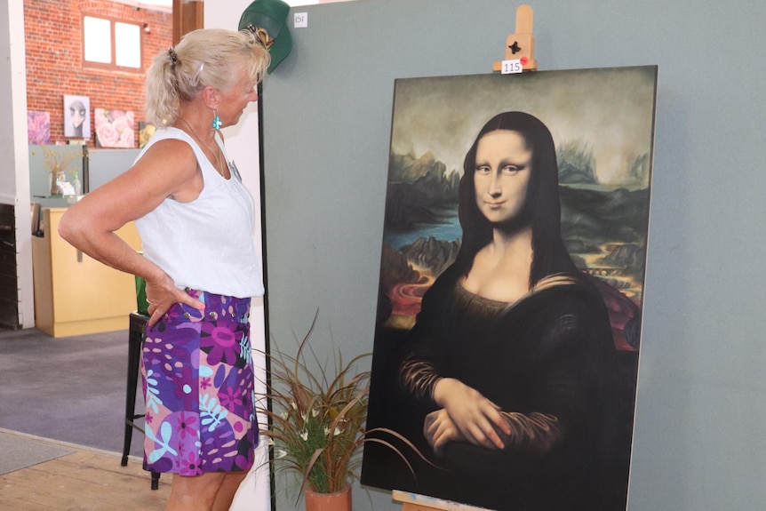 A woman stands looking at a replica of the Mona Lisa painting.