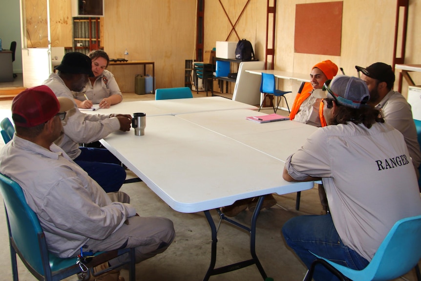 A group of six First Nations rangers sit around a table.