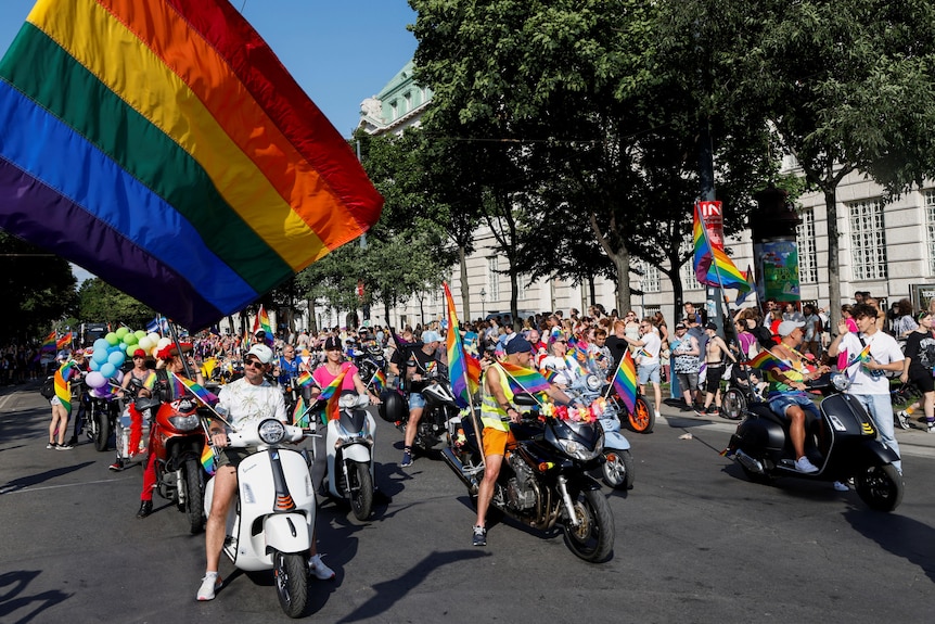 People on motorbikes decorated with pride flags line up in rows for a parade 