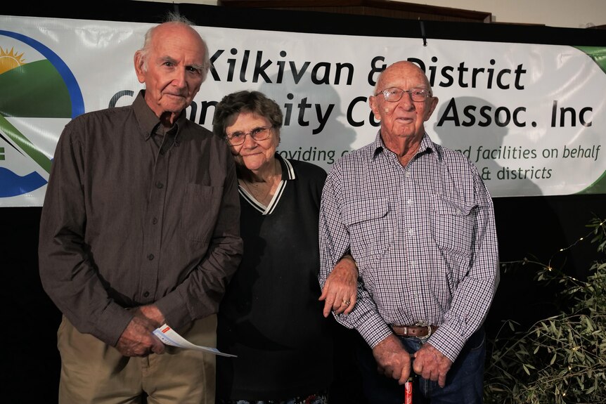 Two men and one woman in the centre all in their 90s smile at the camera