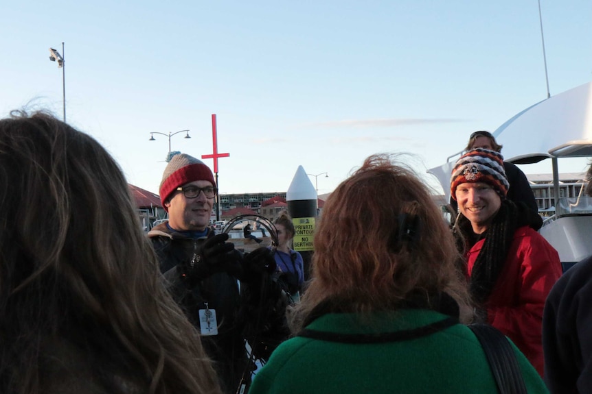 A man passes a pair of headphones to some women, another man waits off to the side.