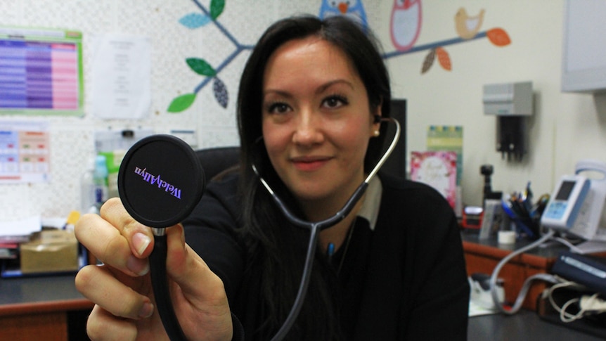 Michelle Ng sitting in her Glenden practice with a stethoscope held up to the camera