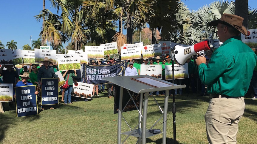 A man with a megaphone stands in front of a crowd people holding placards at a protest.