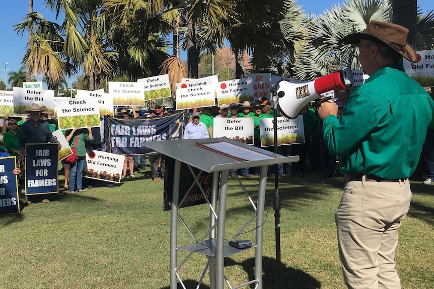 A man with a megaphone stands in front of a crowd people holding placards at a protest.