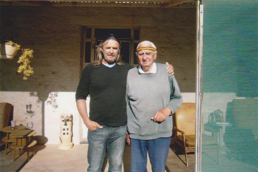 An Indigenous man with long hair and a ponytail, standing next to an older Indigenous man.