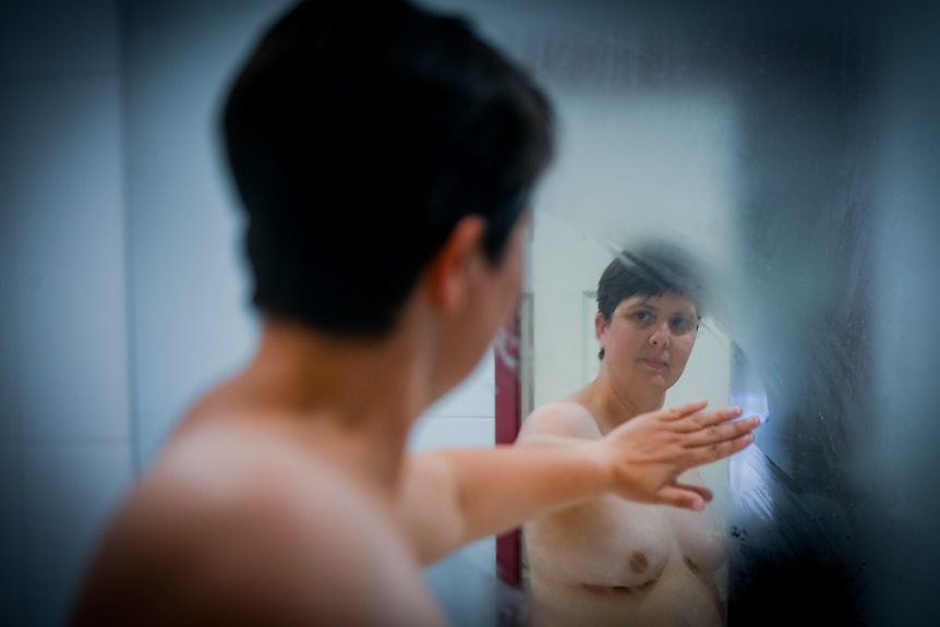 Nicola MacGee wipes condensation away as she looks at herself topless in the mirror.