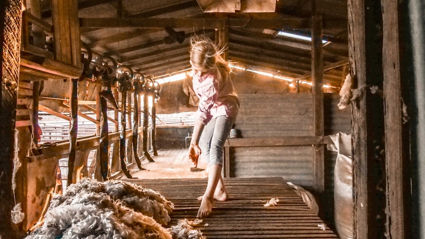 A young girl dressed in country work clothes dances on a bench in a shed