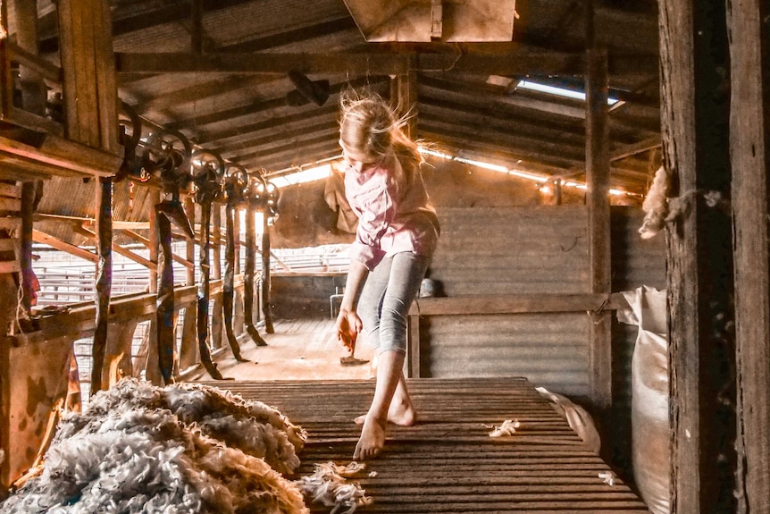 A young girl dressed in country work clothes dances on a bench in a shed