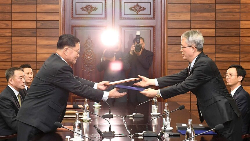 Wide shot of two men exchanging documents over a table.