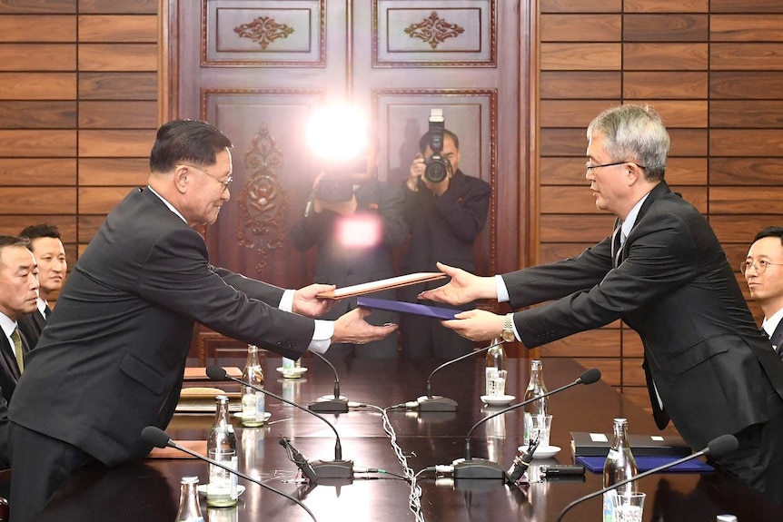 Wide shot of two men exchanging documents over a table.