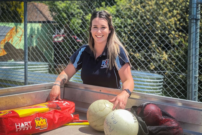 A young woman puts sporting equipment in a ute