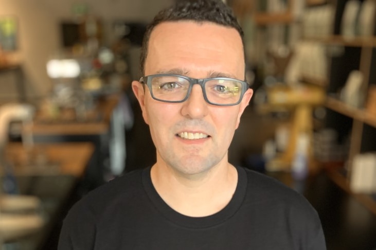 Dave Makin stands, smiling, inside his coffee roasting business in a black t-shirt.