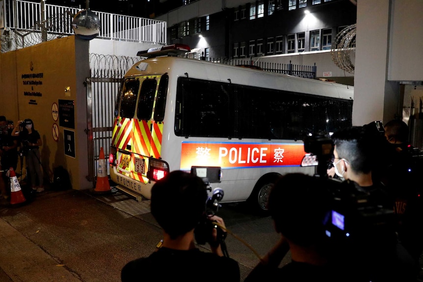 A police van enters through the gates of a Hong Kong police station as reporters record footage.