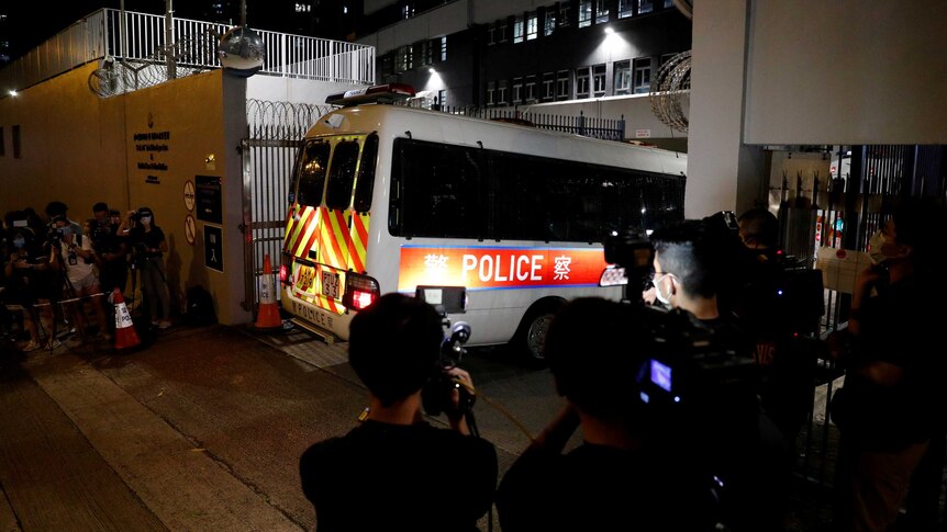 A police van enters through the gates of a Hong Kong police station as reporters record footage.
