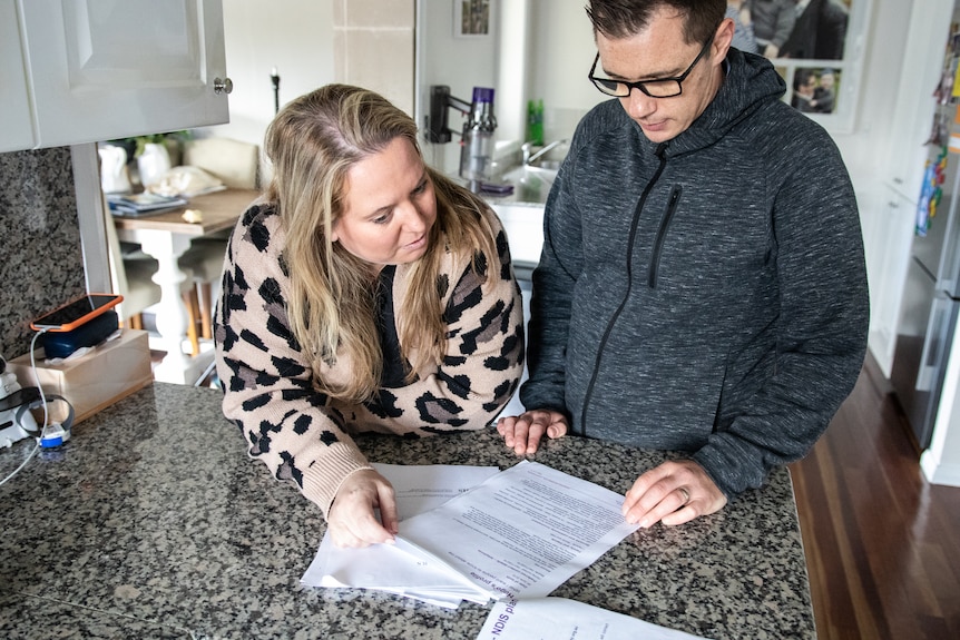 A woman and a man in glasses looking at documents on a kitchen counter.