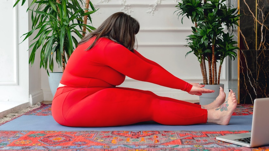 A woman wearing red activewear reaches for her toes on the ground.