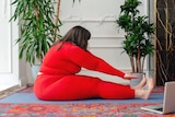 A woman wearing red activewear reaches for her toes on the ground.