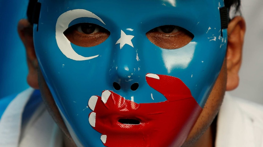 A man wears a mask with the blue East Turkistan flag on it during a protest.