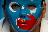 A man wears a mask with the blue East Turkistan flag on it during a protest.